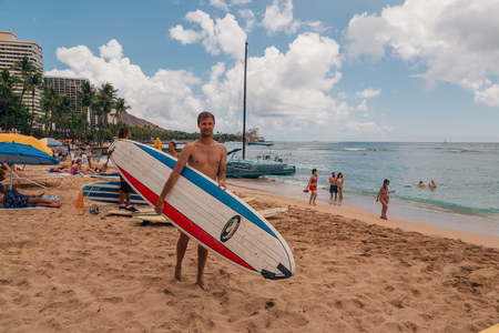 Young man surfer standing on the Waikiki beach in Hawaii with a surf board ready to go surfing. Honolulu, USA. August 30, 2017.のeditorial素材
