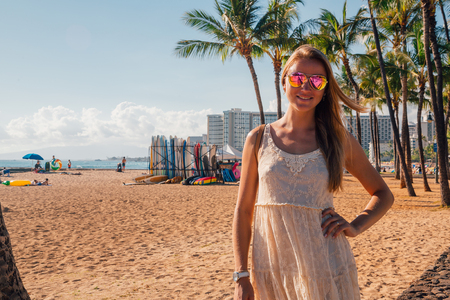 Young girl in a dress walking down the Honolulu Waikiki beach area among palms, surf boards and other people. Honolulu, USA. August 30, 2017.の写真素材