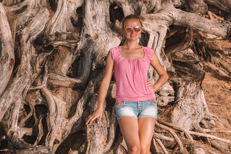 Young girl standing by the huge old tree on the beach on the island of Kauai, Hawaii. Beautiful nature by the people.の写真素材