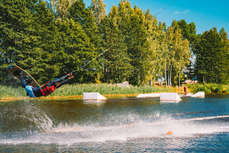 Marupe, Latvia. July 20, 2018. Young man wakeboarding on a lake, making raley, frontroll and jumping the kickers and sliders. Wakeboard.のeditorial素材