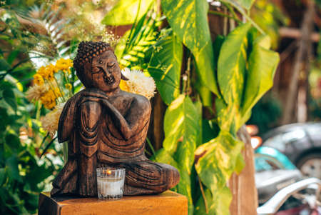 Beautiful seated buddha statue with burning candle in front of leavesのeditorial素材