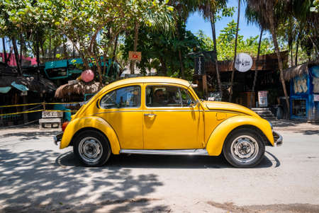 Man riding vintage classic car in front of shops and restaurant