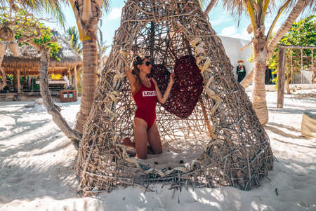 Woman in swimsuit kneeling inside wicker tent at beautiful beach resortのeditorial素材