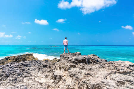 Rear view of man standing of rocks and looking at sea and sky