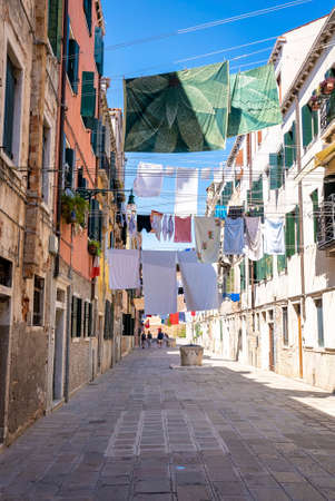 Wet clothes drying on clothesline above alley between residential buildings.の写真素材