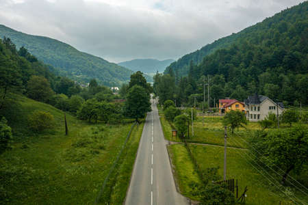 Road going through the village, mountains and forest in the summer time.の写真素材
