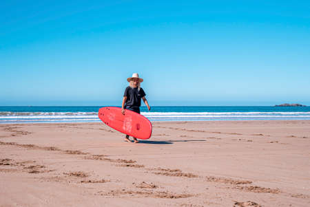 Smiling male surf teacher carrying surfing board while walking on beachの写真素材