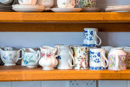 Assortment of hand painted ceramic floral pattern teacups with mugs on shelves