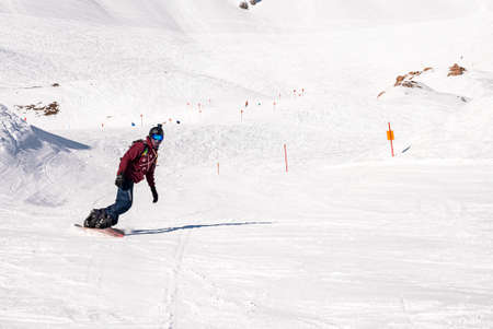 Young snowboarder sliding down snowy slope on mountain at winter resortの写真素材