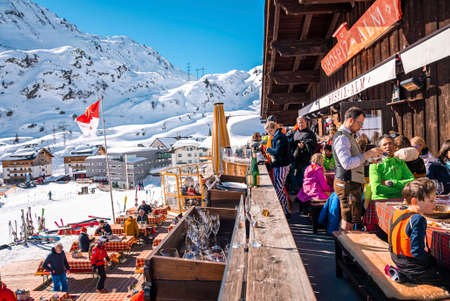 People sitting at mountain cafe beside tables on sunny day during skiing holidayの写真素材