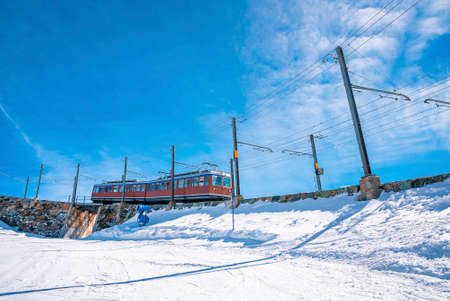 Red train moving towards gornergrat station on mountain against blue skyの写真素材