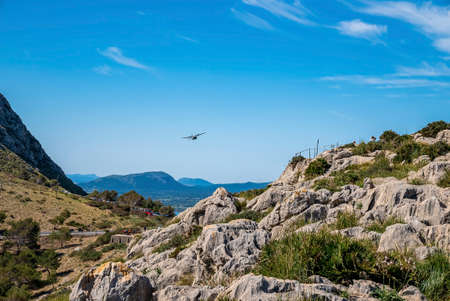 Airplane flying over rocky mountain at island against blue skyの写真素材