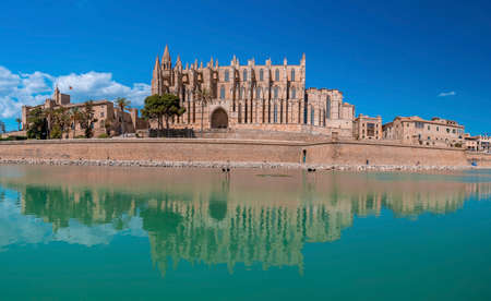 Famous medieval La Seu Cathedral reflecting in canal water against blue skyの写真素材