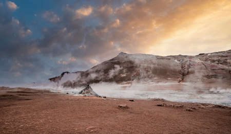 Steam emitting from crater in geothermal area of Hverir against sky during sunsetの写真素材
