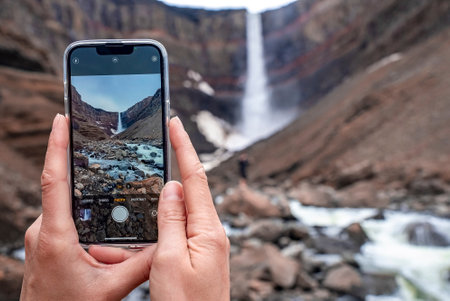Cropped image of tourist traveler photographing Hengifoss waterfall on cellphoneの写真素材