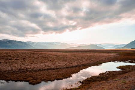 View of stream flowing amidst landscape in volcanic valley against cloudy skyの写真素材