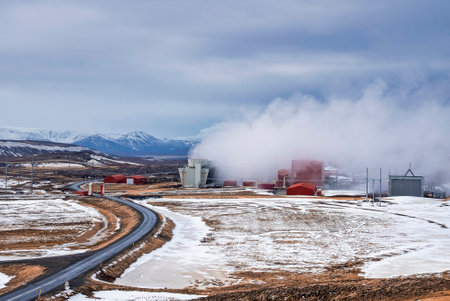 Steaming cooling tower at Krafla geothermal power plant by road against skyの写真素材