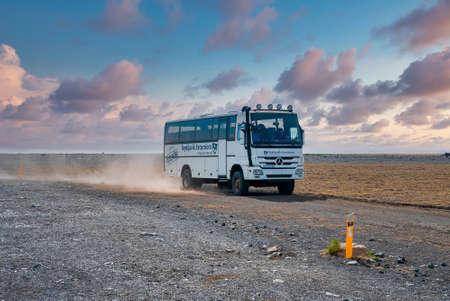 Reykjavik Excursions bus moving on lava sand at volcanic highland against skyの写真素材