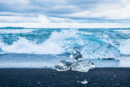 Iceberg chunk on black sand with waves rushing in background at Diamond beach