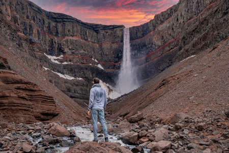 Tourist standing on rock while looking at Hengifoss waterfall during sunsetの写真素材