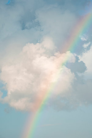 Scenic view of rainbow amidst fluffy clouds in sky on sunny dayの写真素材