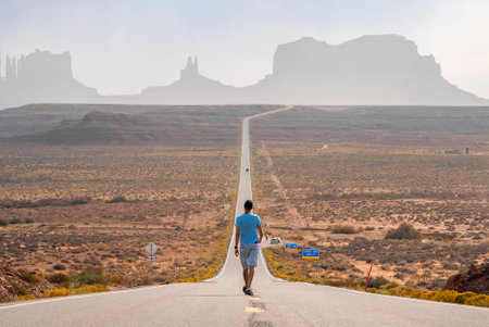 Male tourist walking on road leading towards Monument valley during summerの写真素材