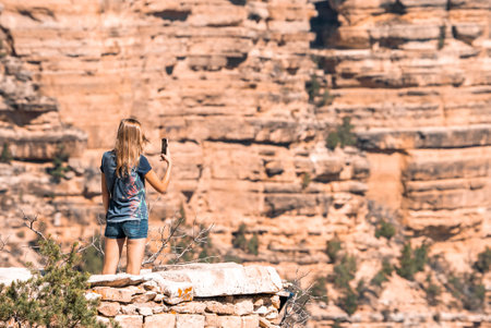 Rear View Of Woman Photographing Rocky Mountain With Smartphone