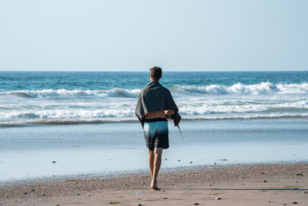 Rear view of man with towel walking at beach during summerの写真素材