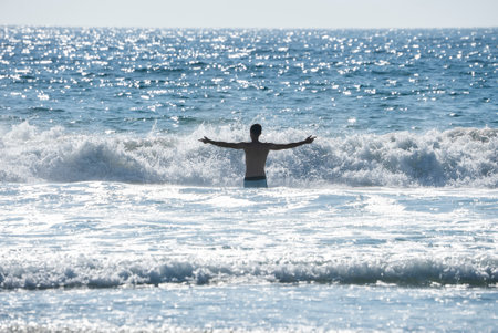 Carefree shirtless man with arms outstretched standing amidst seaの写真素材