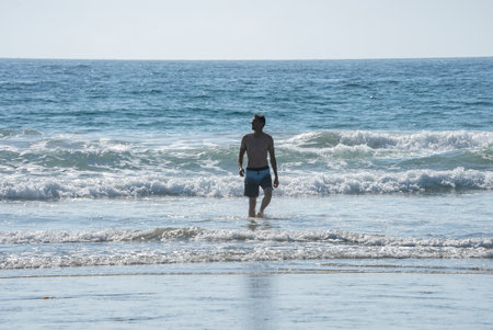Shirtless man walking amidst waves during vacation on sunny dayの写真素材