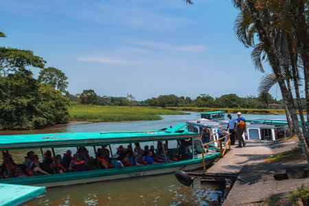 Tourists boarding boat moored beside pier on river with green landscape under sky