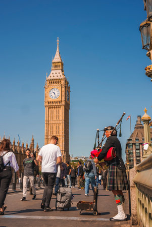 Senior man playing bagpipe amidst Tourists walking by Clock Tower