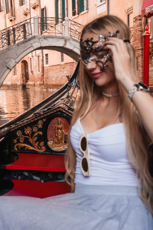 Woman wearing traditional Venetian mask rides gondola through scenic canals of Venice, Italy.の写真素材