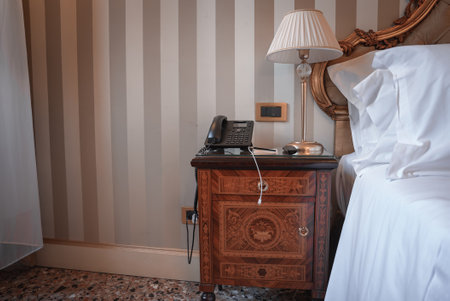 Classic bedroom with wooden bed frame, nightstand, and lamp. Neutral color scheme creates a calming atmosphere. Traditional Venetian style fits in with the collection.の写真素材