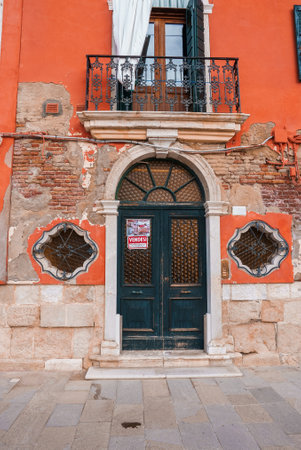 A charming orange building featuring a black ornate door, decorative balcony, and weathered brick facade with unique architectural details and stone accents.の写真素材