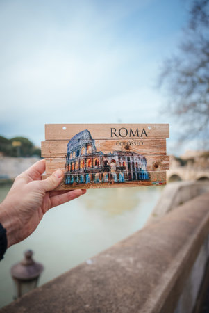 Hand holding Colosseum postcard aligning with background, ROMA COLOSSEO, in overcast Rome.
