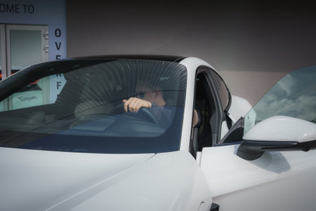 Close up view of white car with drivers side door ajar, hand gripping steering wheel.