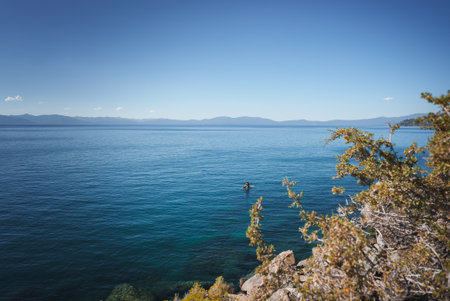 Tranquil lakeside scene with kayaker, mountains, and clear blue sky