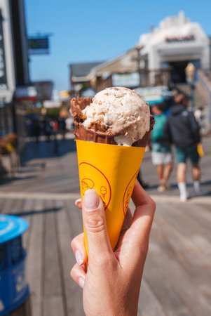 Hand holding smiley ice cream cone on busy San Francisco street