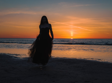 Happy beautiful woman in a long black dress enjoying beautiful sunset on the Beach in California.の写真素材