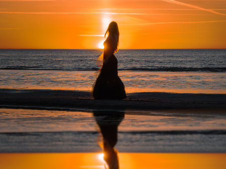 Happy beautiful woman in a long black dress enjoying beautiful sunset on the Beach in California.の写真素材