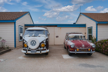 Vintage VW Bus and MGB GT parked in front of coastal building, possibly along the Californian coast.