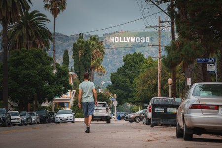 Explore a scene in a Los Angeles neighborhood as a person walks towards the iconic Hollywood sign,...