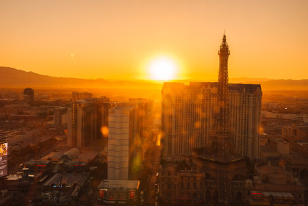 Aerial view of Las Vegas Strip at sunset. Sun bathes scene in golden hues, iconic buildings' silhouettes highlighted. Sky transitions orange to blue. Nightlife hints. Mountain contrast.の写真素材
