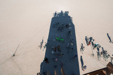 Festival scene in desert with long shadow, people and bicycles under vibrant colors