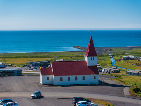 Aerial View of White Church with Red Roof Overlooking Black Sand Beach in Icelandの写真素材