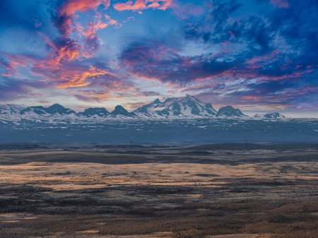 Snow-Capped Mountain Range with Vibrant Sky and Barren Landscape in Icelandの写真素材