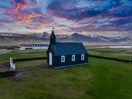 Aerial View of Black Church with Snow-Capped Mountains and Vibrant Sky in Icelandの写真素材
