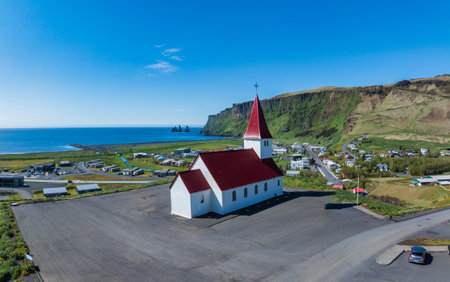Aerial View of White Church with Red Roof Overlooking Black Sand Beach in Icelandの写真素材