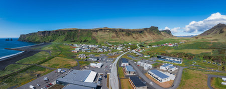 Aerial View of Icelandic Town Between Black Sand Beach and Mountains